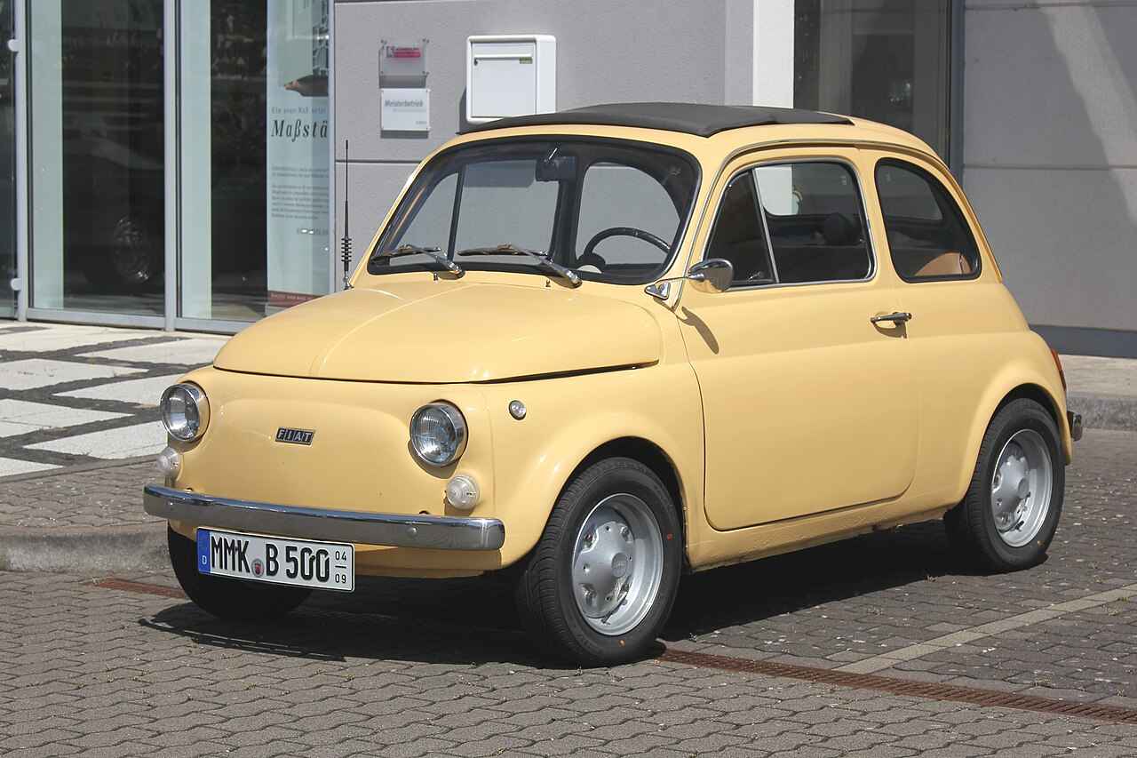 Fiat 500 com design clássico estacionado em frente a um prédio moderno.